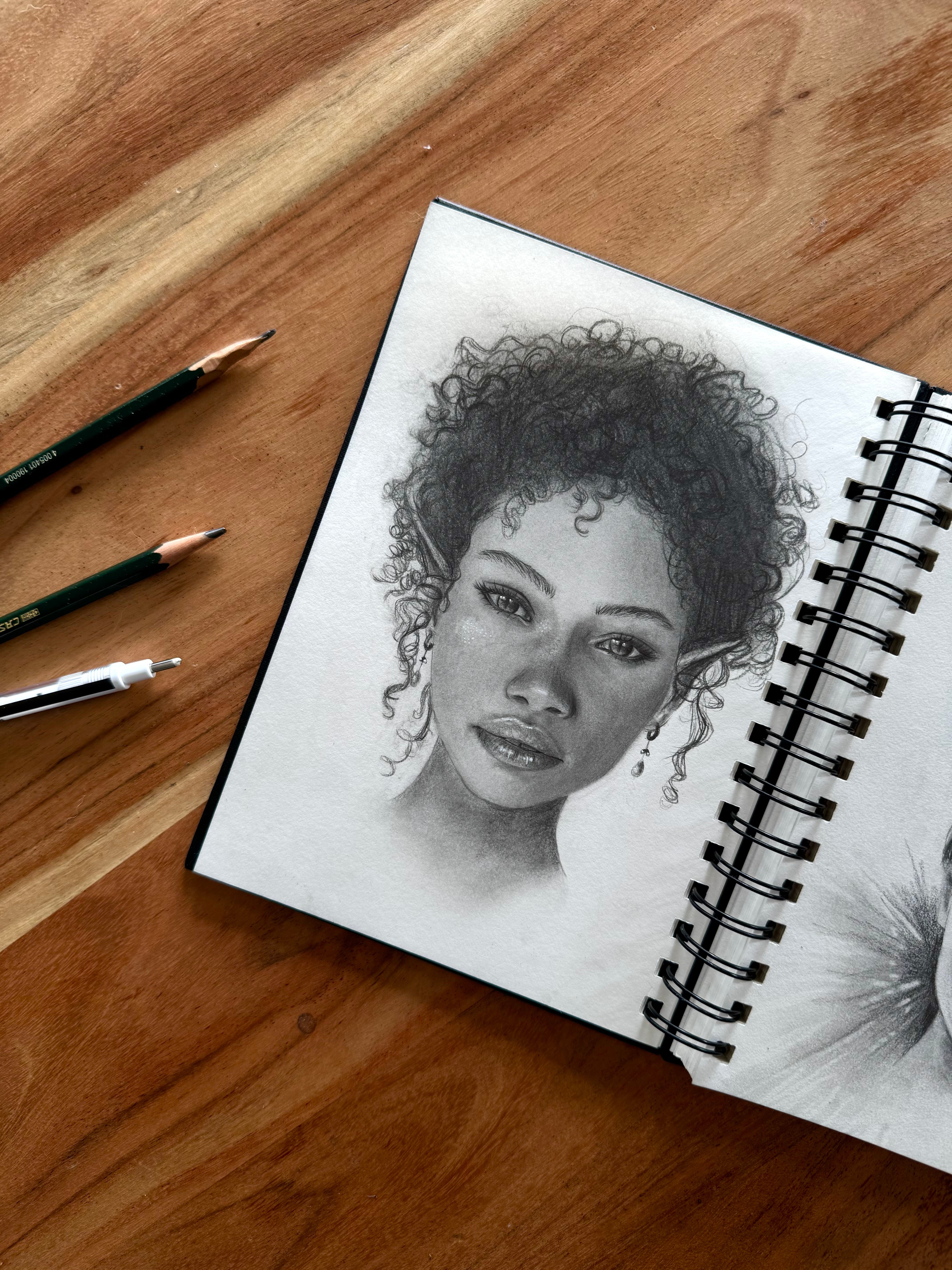 Croquis d’une elfe aux cheveux bouclés dans un carnet, représentant un portrait détaillé en noir et blanc